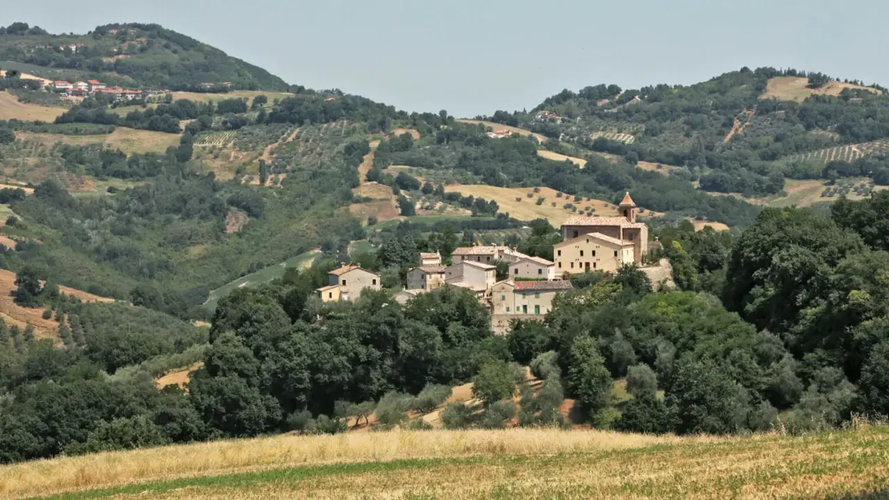 Borgo collinare di **Cerreto di Saludecio** con case in pietra e una chiesa, immerso nel verde della campagna romagnola.