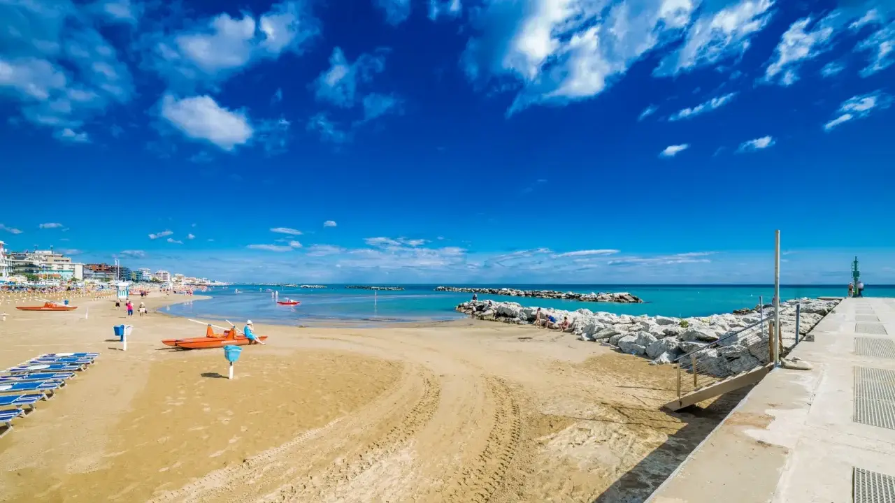 Spiaggia di Bellaria Mare con lettini, bagnini arancioni e mare azzurro sotto un cielo blu con nuvole bianche.