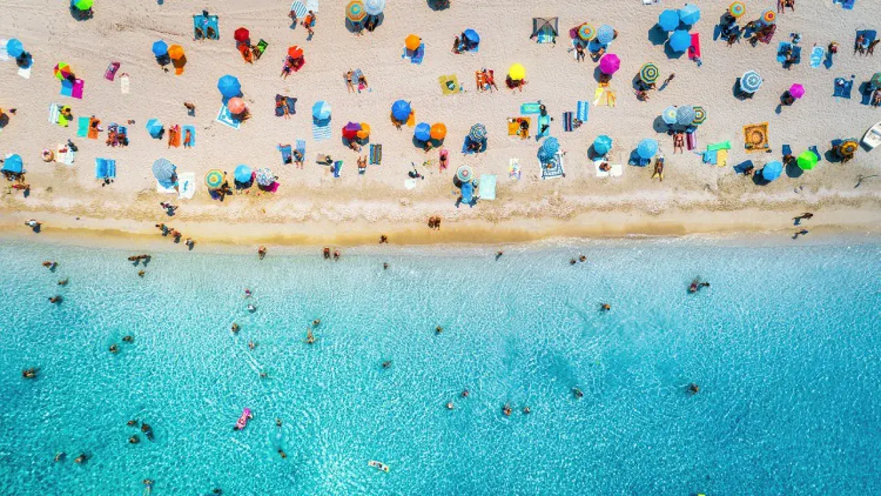 Un'affollata spiaggia di Rimini mare, con ombrelloni colorati e bagnanti che si godono il sole e il mare cristallino.