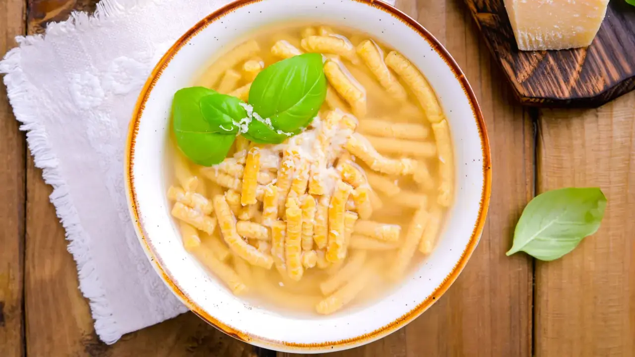 Piatto di passatelli in brodo, un classico dei piatti romagnoli, guarnito con basilico fresco e parmigiano.