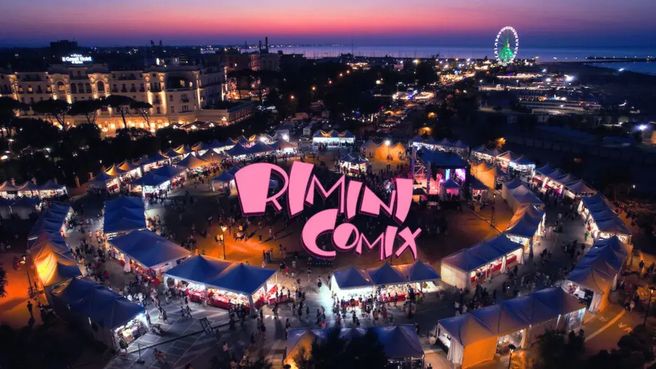 Un vivace evento serale a Rimini Comix, con bancarelle illuminate, una ruota panoramica e il logo rosa che domina la scena.