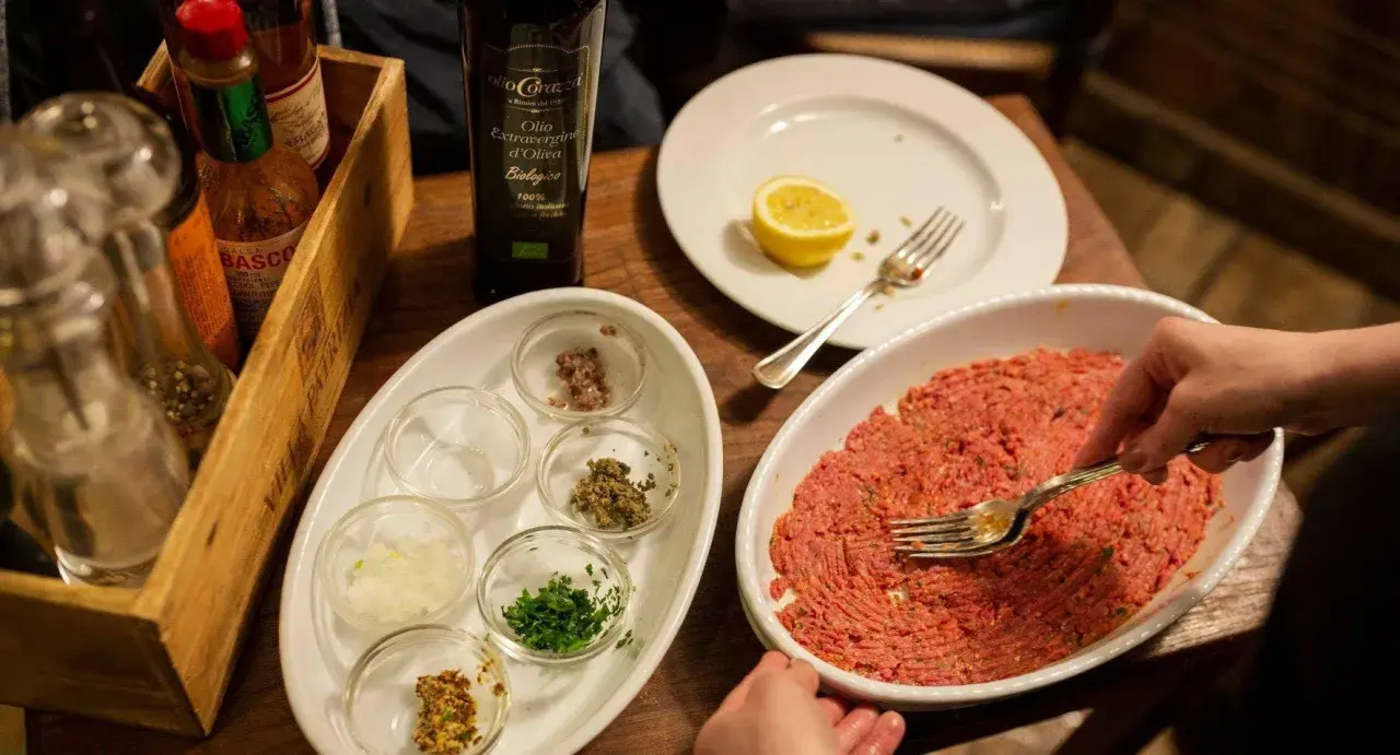 Preparazione di tartare di carne in un ristorante a Rimini, con condimenti e olio EVO.