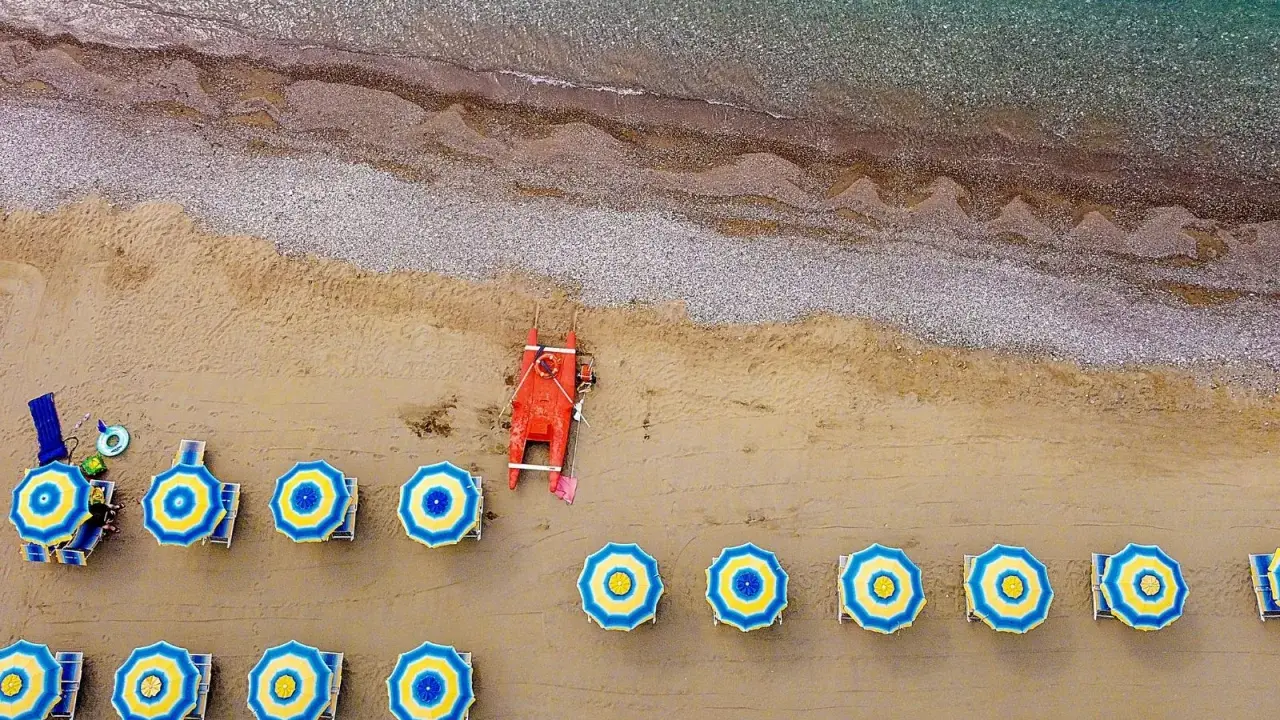 Ombrelloni blu e gialli e una barca rossa sulla spiaggia di Misano Marittima, con il mare turchese sullo sfondo.