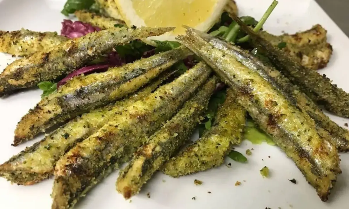Sardoncini alla romagnola dorati e croccanti, serviti su un letto di insalata fresca con una fetta di limone.