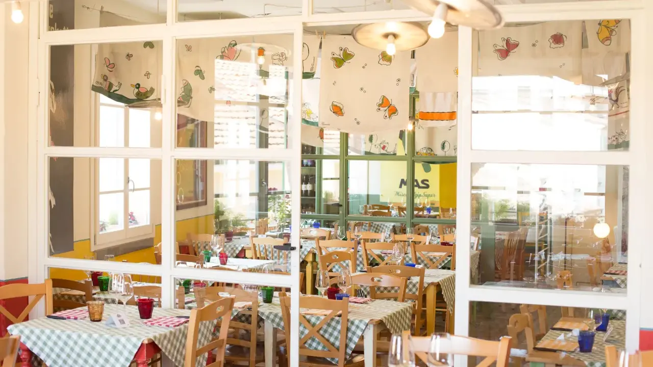 Interno di un'osteria de borg con tavoli apparecchiati con tovaglie a quadretti verdi e bianchi, sedie in legno e decorazioni colorate.