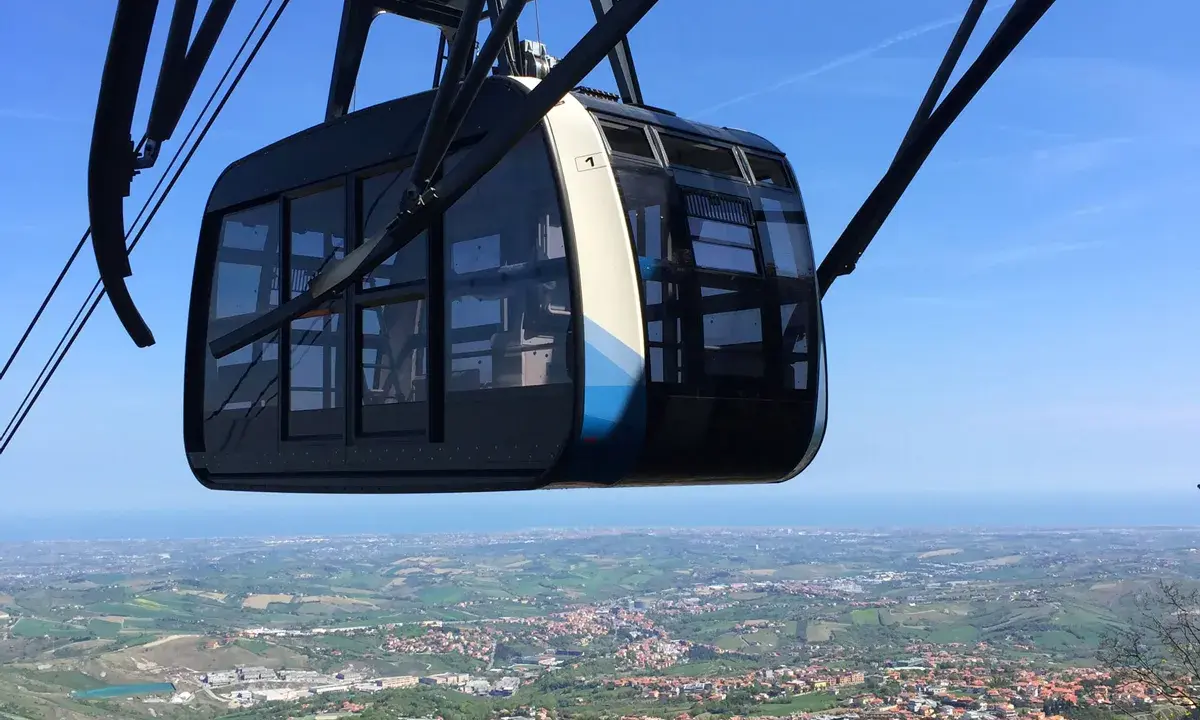 Cabina della funivia di San Marino in primo piano, con vista panoramica sulla città e sul mare all'orizzonte.