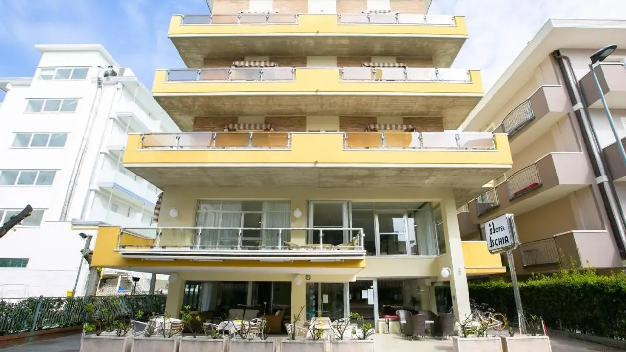 Hotel Ischia a Rimini Marebello, con le sue terrazze gialle e le finestre luminose, pronto ad accogliere i suoi ospiti per una vacanza al mare.