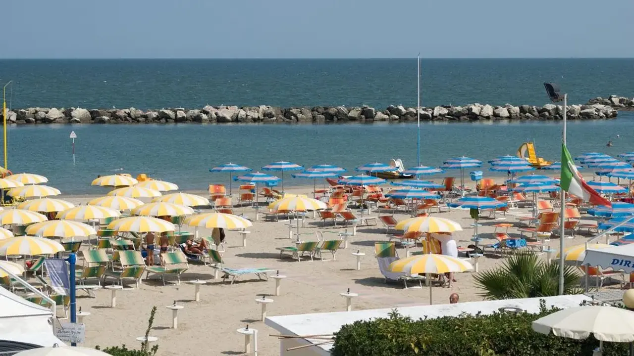 Spiaggia affollata con ombrelloni gialli e bianchi, lettini e il mare azzurro. Un'immagine di igea marittima, perfetta per una vacanza.