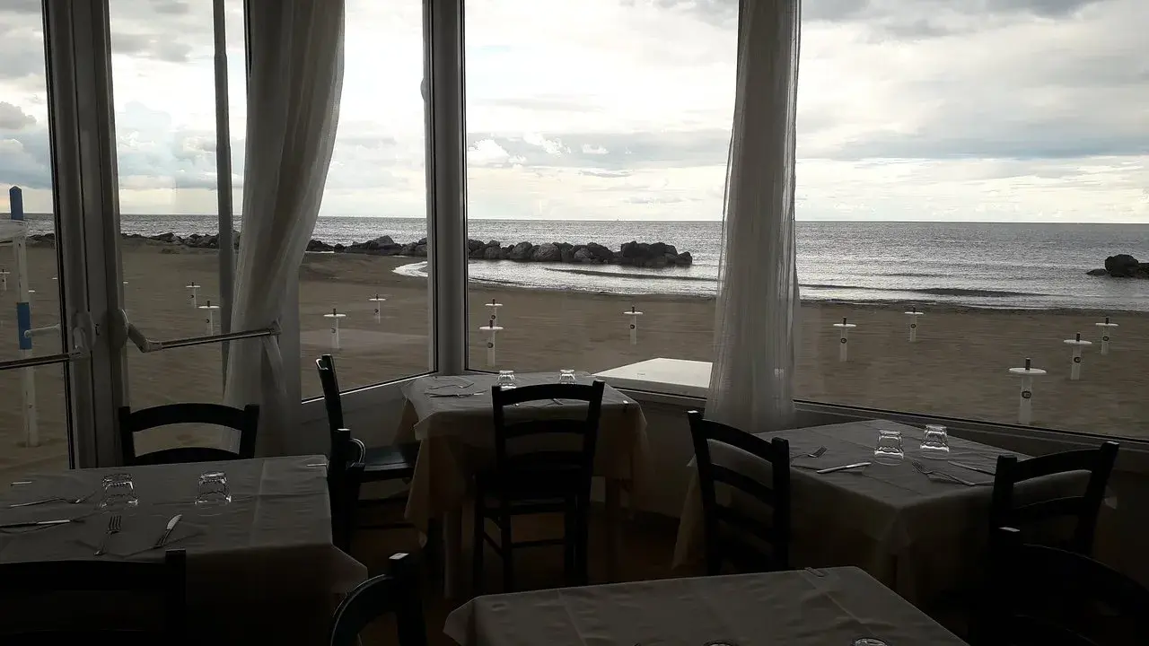 Tavoli apparecchiati in un ristorante con vista sulla spiaggia di Misano durante la bassa marea.