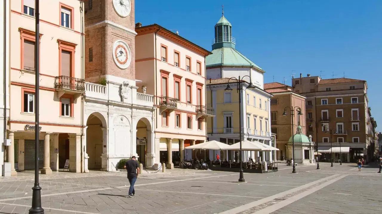 Passeggiata nella soleggiata piazza Tre Martiri a Rimini, con i suoi palazzi storici e il caratteristico orologio.