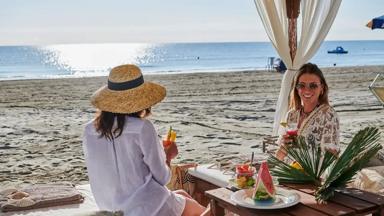 Due donne sorseggiano cocktail in un bagno Jacarè a Cervia, godendosi la spiaggia e il mare.