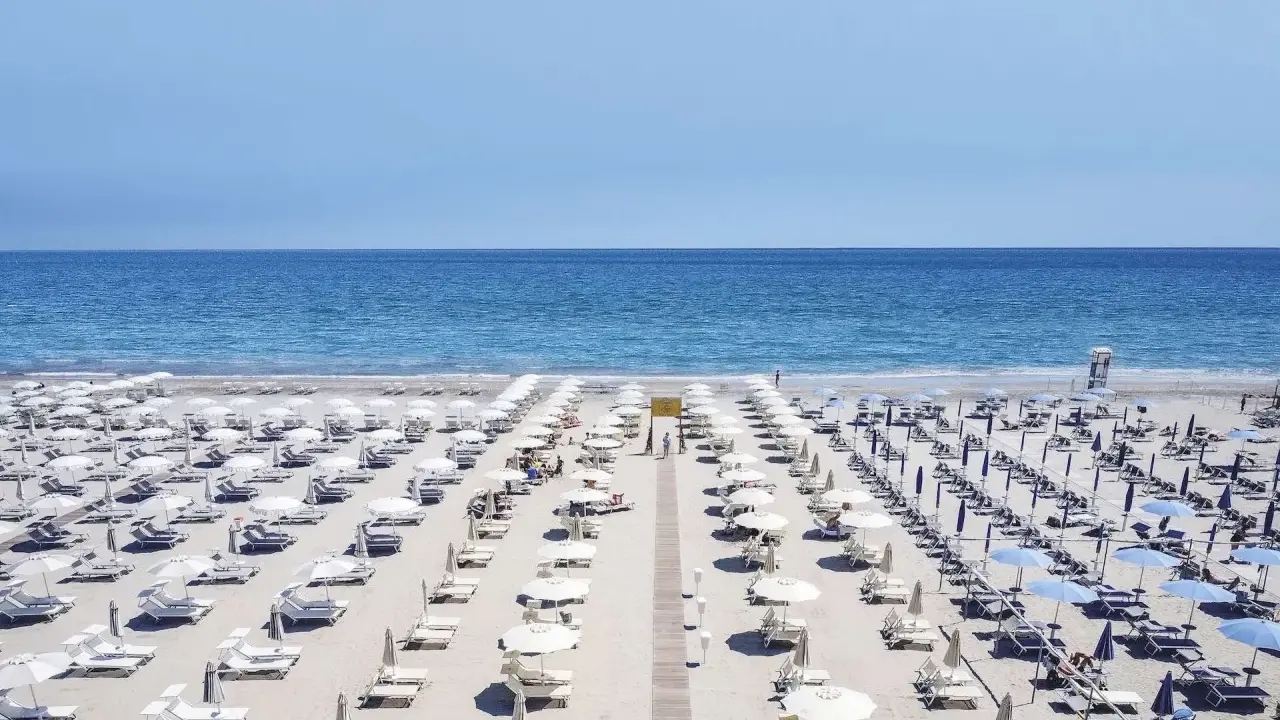 File di ombrelloni bianchi e lettini ordinati sui **stabilimenti balneari Cervia**, con il mare azzurro sullo sfondo.