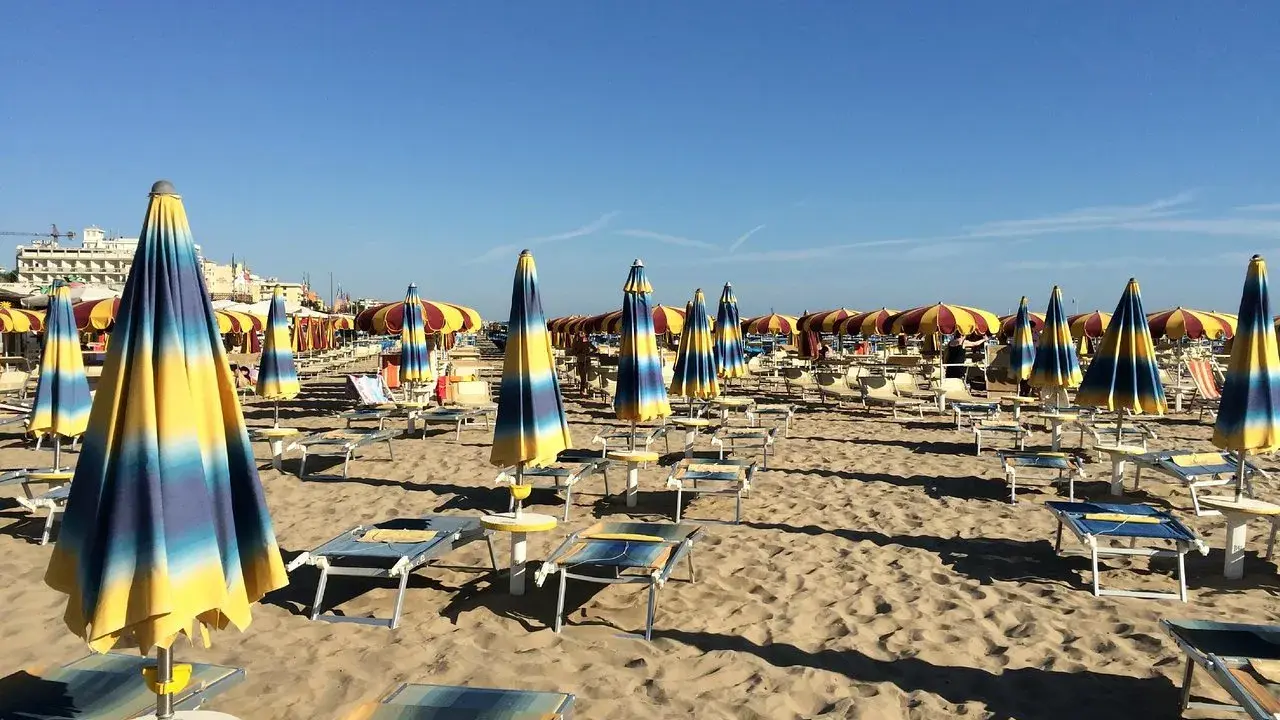 Ombrelloni a righe blu e gialle e lettini vuoti sulla spiaggia di Rivazzurra, in attesa dei bagnanti.