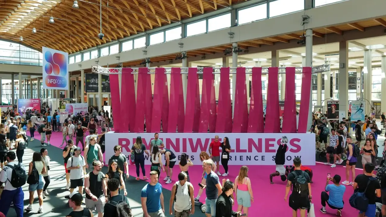 Folla animata a Rimini Wellness, un evento dedicato al benessere e al fitness. Persone di ogni età passeggiano tra gli stand e le aree espositive.