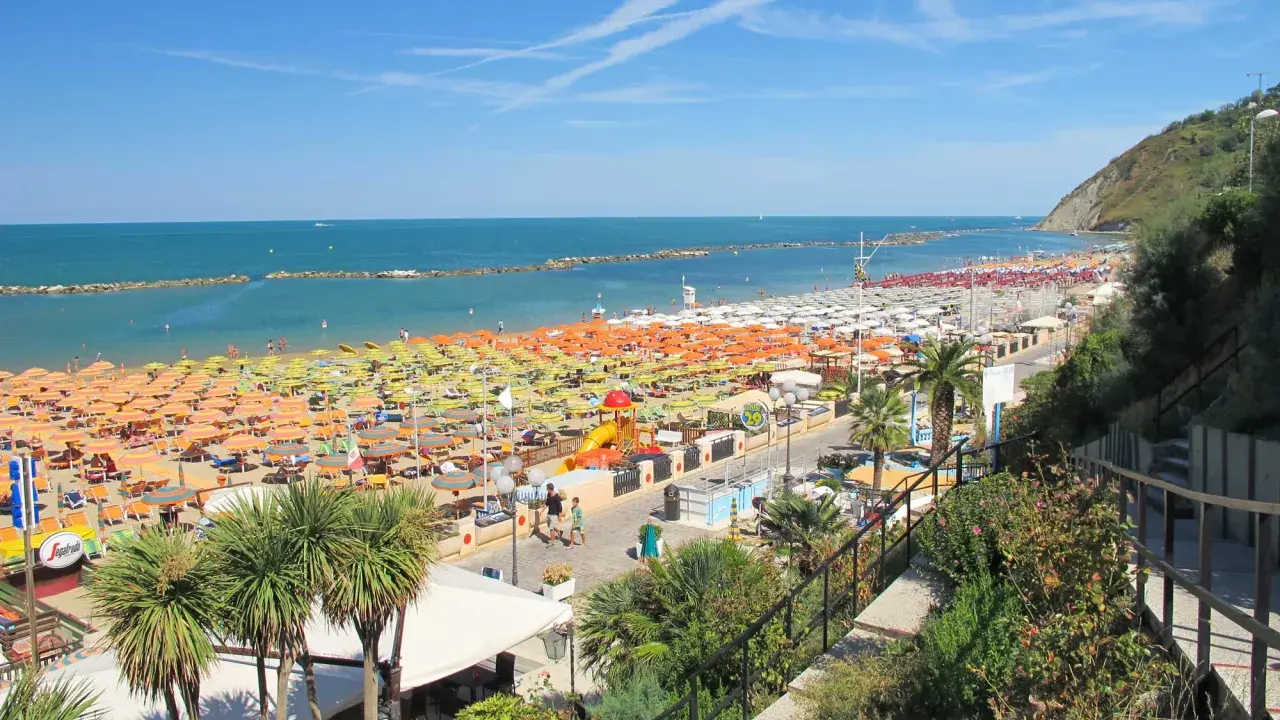 Spiaggia affollata a Gabicce Mare, con file infinite di ombrelloni colorati e lettini. Le recensioni la descrivono come un paradiso estivo.