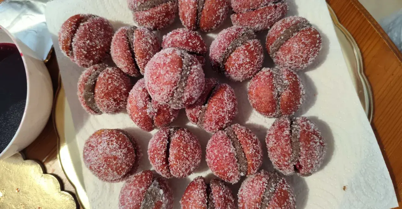 Dolci castagnole romagnole, due semisfere rosse unite da una crema scura e ricoperte di zucchero.