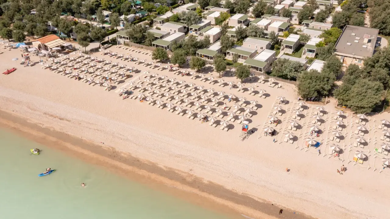 Domenica di sole sulla spiaggia di Rivazzurra, con ombrelloni, lettini e bagnanti che si godono il mare.