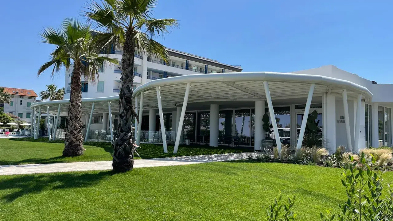 Palme e prato verde davanti a un moderno ristorante a Bellaria Igea, con un edificio bianco sullo sfondo.