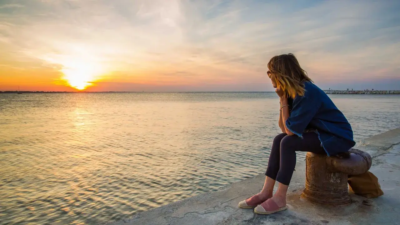 Donna seduta osserva il tramonto a Rimini, con il sole che si riflette sul mare calmo.