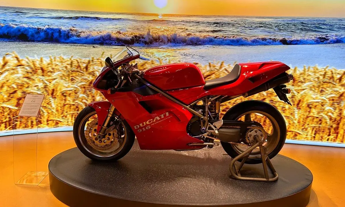 Ducati rossa su un palco, con sfondo di un campo di grano e il mare al tramonto. Un connubio perfetto tra la piada e il mare.