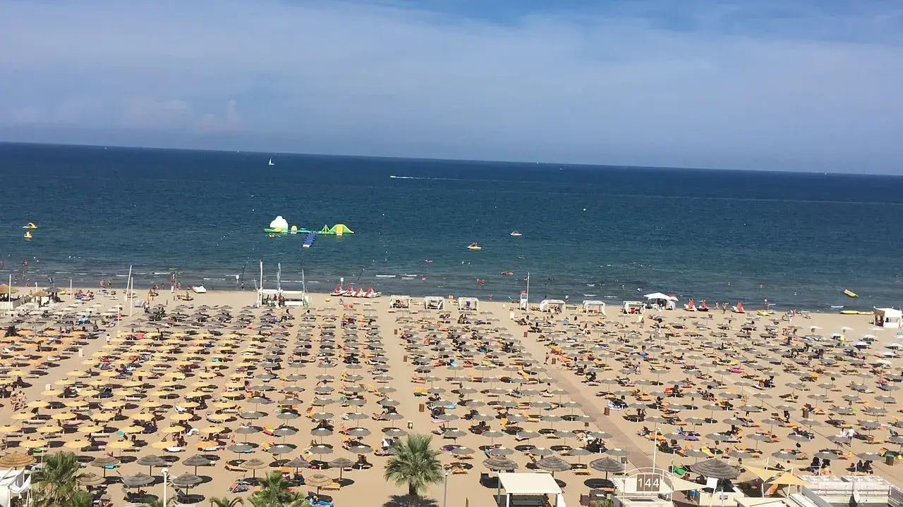 Una vasta spiaggia di Miramare gremita di ombrelloni e lettini, con bagnanti che si godono il sole e il mare azzurro.