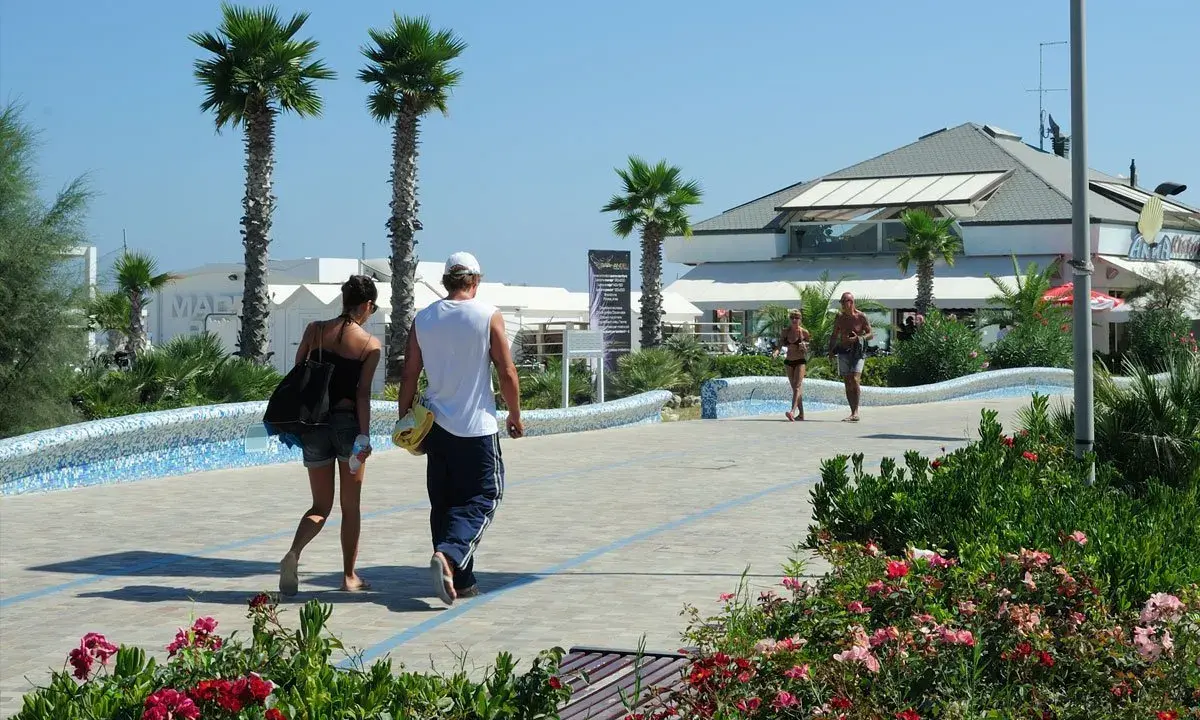 Coppia passeggia sul lungomare del parco mare nord Misano, tra palme e fiori.