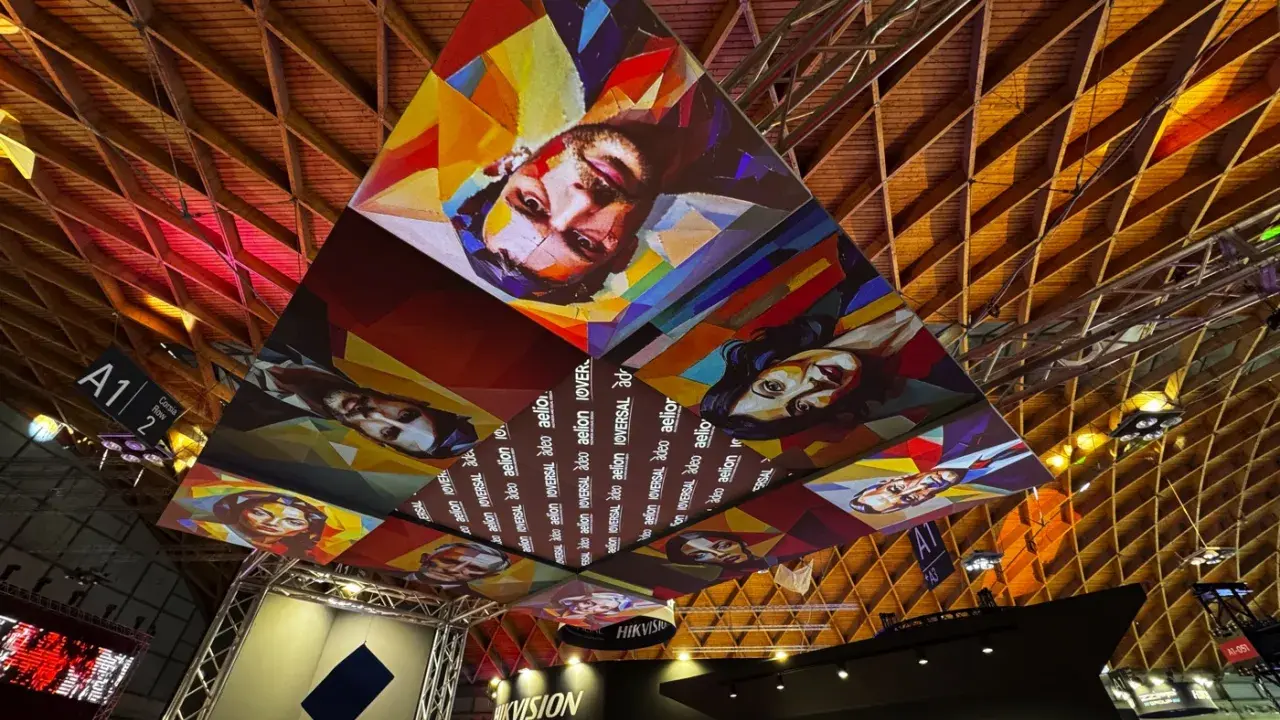 Installazioni artistiche colorate dominano il soffitto di una mir fiera, con volti stilizzati e il logo "Hikvision".