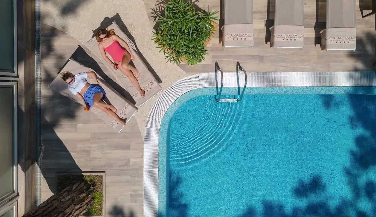 Due donne rilassate a bordo della piscina di Milano Marittima, con lettini e ombrelloni.