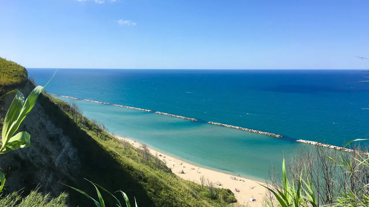Vista panoramica della spiaggia di Fiorenzuola di Focara, con mare azzurro e scogliera verdeggiante.