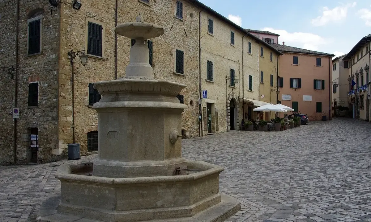 Piazza con fontana in pietra, circondata da edifici storici. Un angolo di pace nei borghi vicino Cattolica.