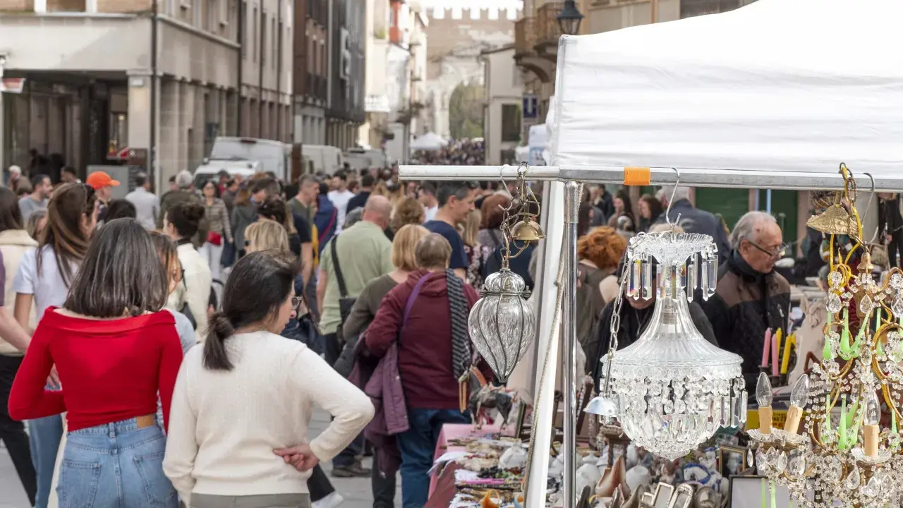 Folla animata in un mercatino usato a Rimini, tra bancarelle con lampadari di cristallo e oggetti d'antiquariato.