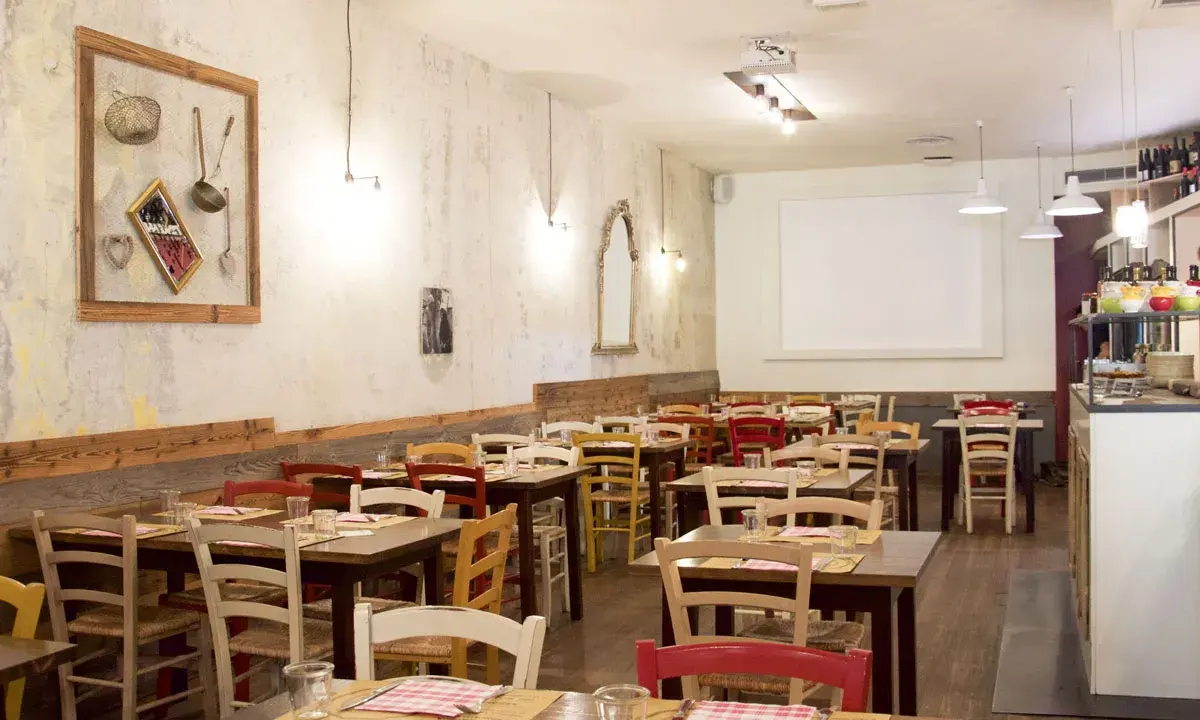 Interno di un ristorante accogliente, con tavoli apparecchiati e sedie colorate. Sembra proprio il posto ideale per una cena da "la mi mama Rimini".