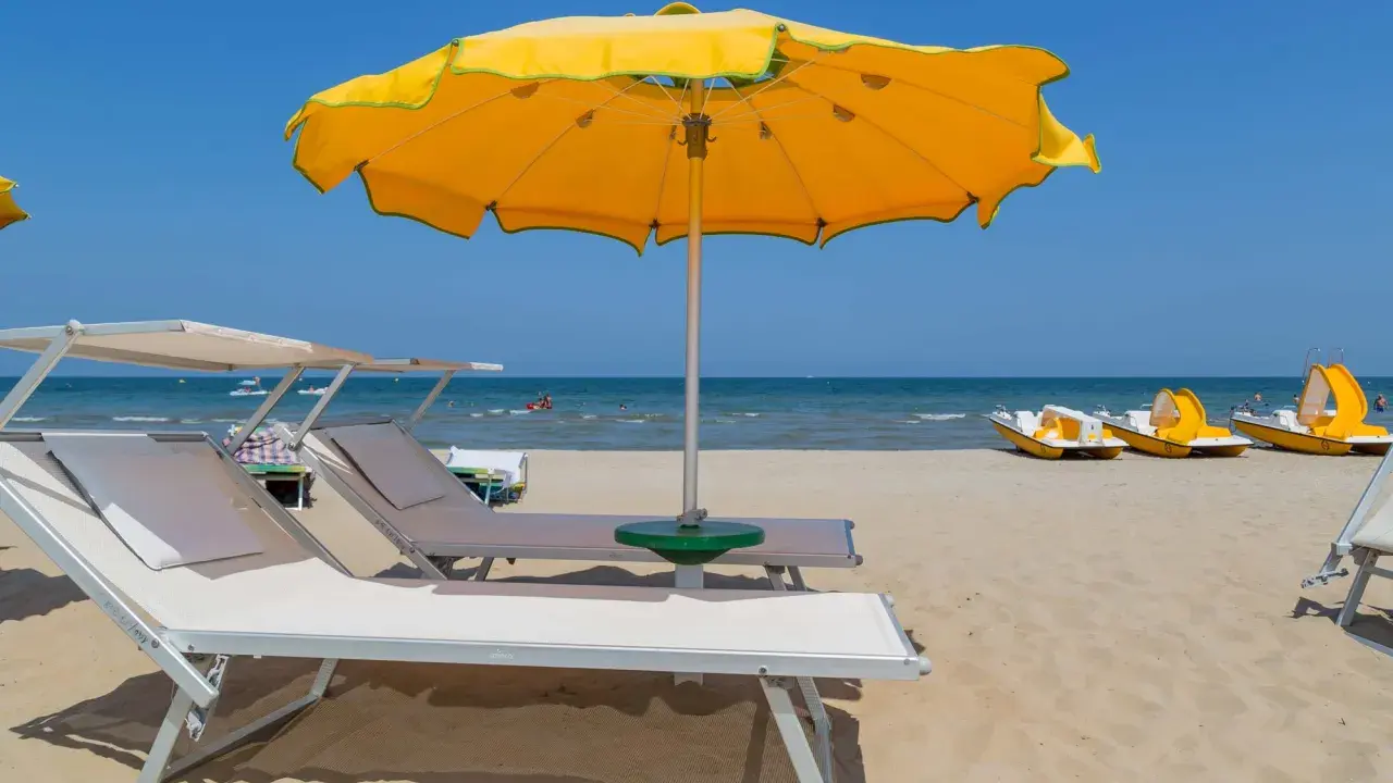 Spiagge di Rimini con lettini, ombrellone giallo e pedalò pronti per l'estate.