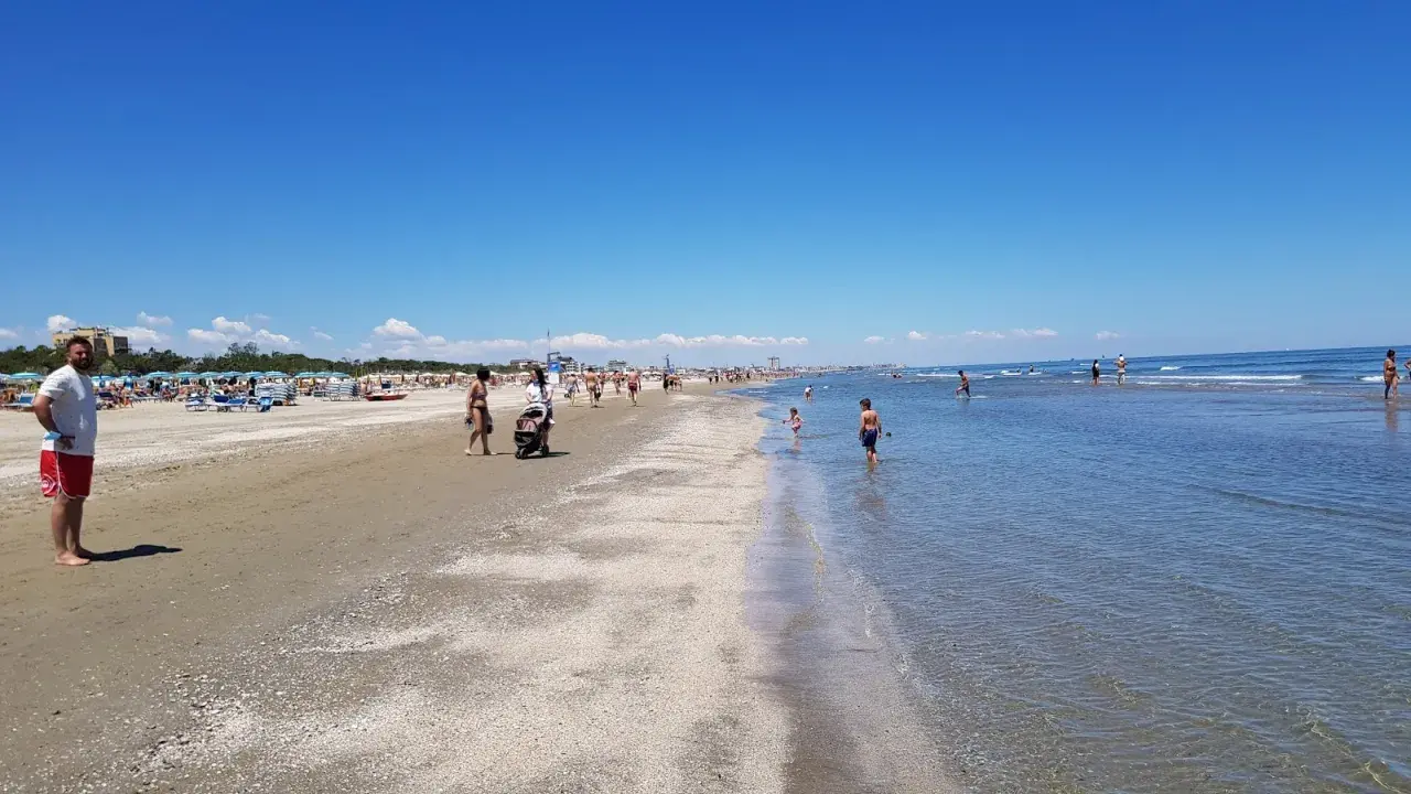 Una giornata di sole a Pinarella di Cervia mare, con bagnanti che passeggiano sulla sabbia e bambini che giocano nell'acqua cristallina.