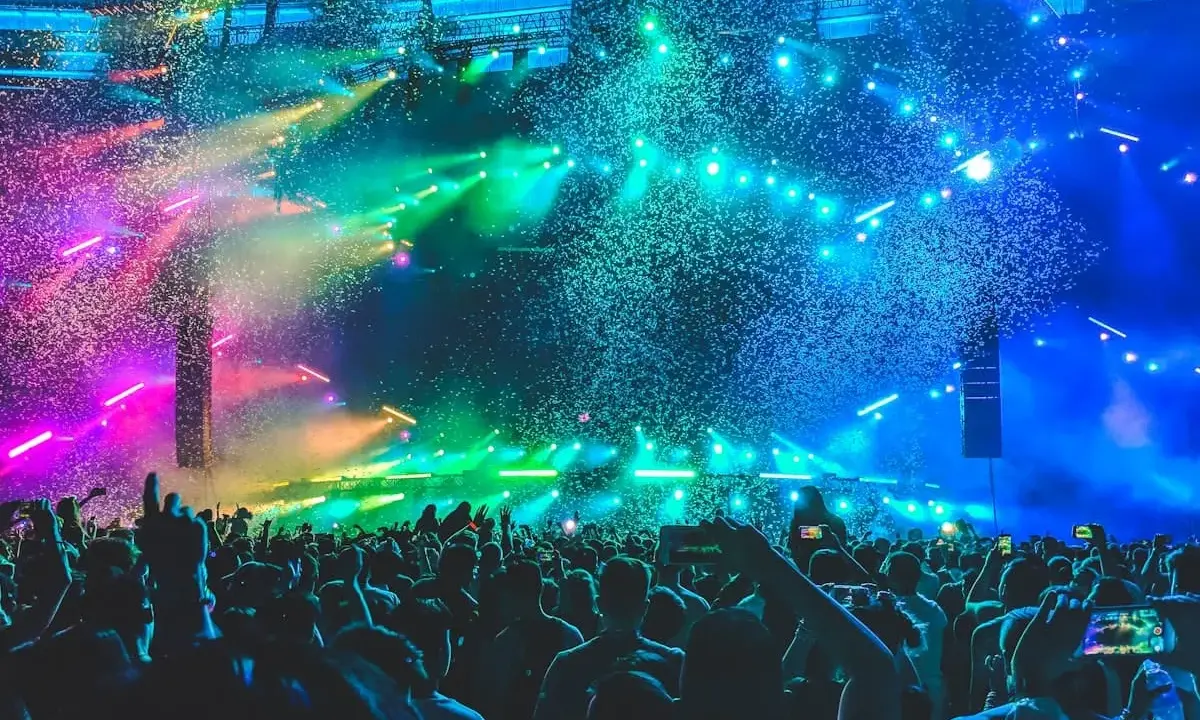 Folla in delirio a un concerto a Rimini, con coriandoli colorati e luci psichedeliche che illuminano la scena.