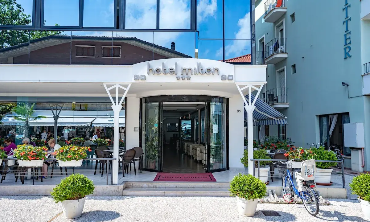 Ingresso accogliente dell'Hotel Milton Valverde con tavolini all'aperto e fiori colorati. Biciclette parcheggiate, pronte per esplorare.