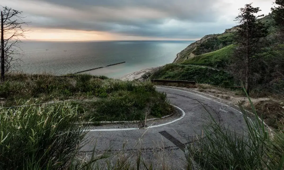 Strada tortuosa sul Monte San Bartolo con vista sul mare Adriatico al tramonto.