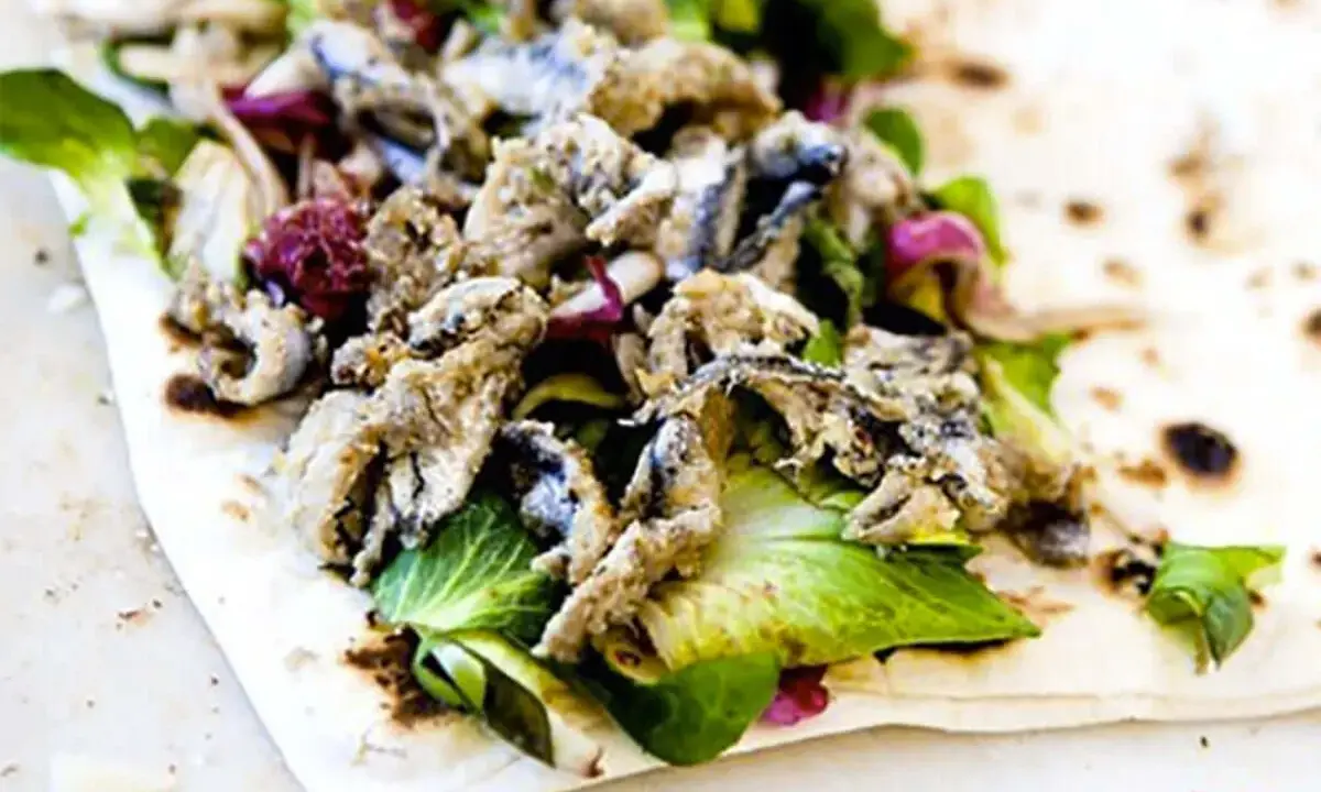 Sardoncini al testo su piadina con insalata fresca e cipolla rossa. Un sapore di mare e terra.