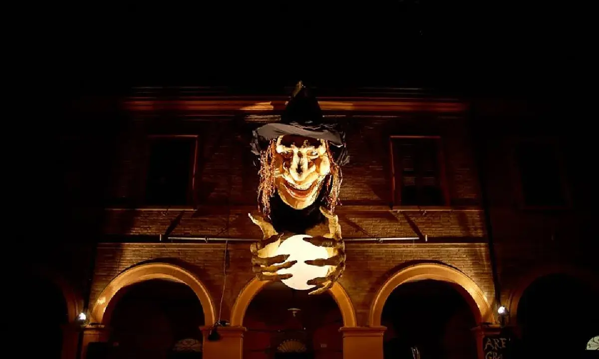 Una strega spaventosa con un cappello nero e una sfera luminosa in mano, illuminata nella notte. Sembra la protagonista de la notte delle streghe.
