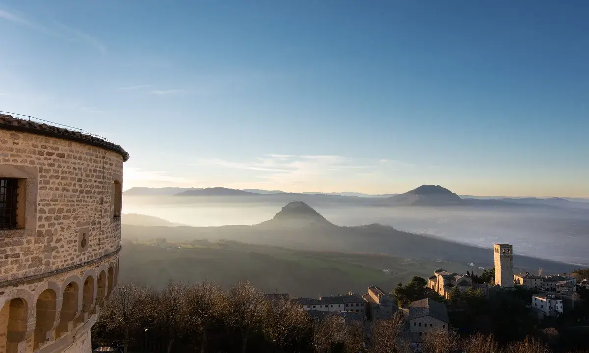 Panoramica di borghi vicino Riccione, con un antico torrione e colline nebbiose all'alba.