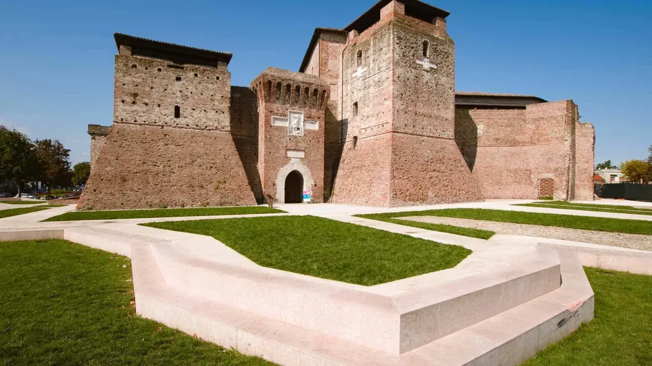 Imponente Castel Sismondo, con le sue torri in mattoni rossi e il cortile verdeggiante, si erge maestoso sotto un cielo azzurro.