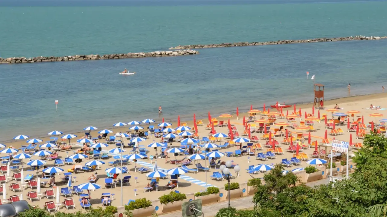 Spiaggia affollata con ombrelloni colorati, lettini e bagnanti. Perfetta idea per sapere dove andare al mare in Emilia Romagna.
