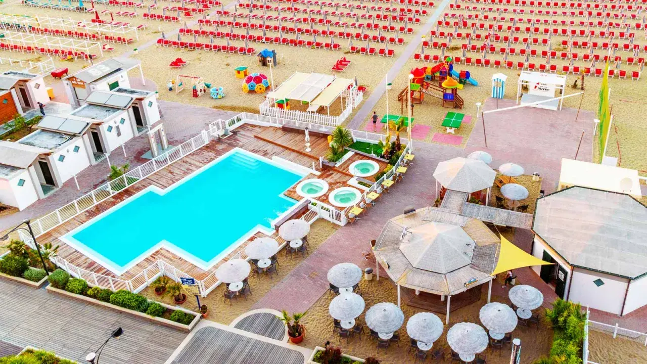 Vista aerea del lido delle sirene Cattolica: piscina, vasche idromassaggio, lettini rossi e ombrelloni sulla spiaggia.