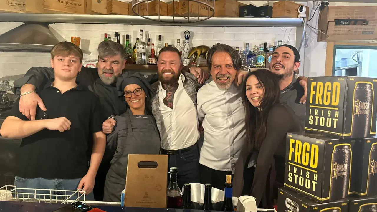 Staff sorridente a Misano Adriatico, con un ragazzo che sembra un gambero sbronzo tra loro. Sul bancone, bottiglie e lattine di "FRGD Irish Stout".