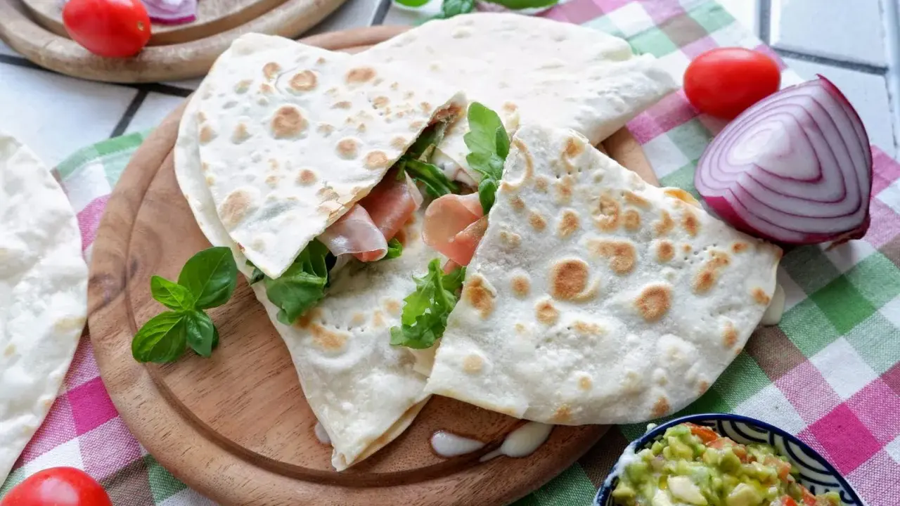 Piadina, piatto tipico di Rimini, farcita con prosciutto e rucola, servita con guacamole e verdure fresche.
