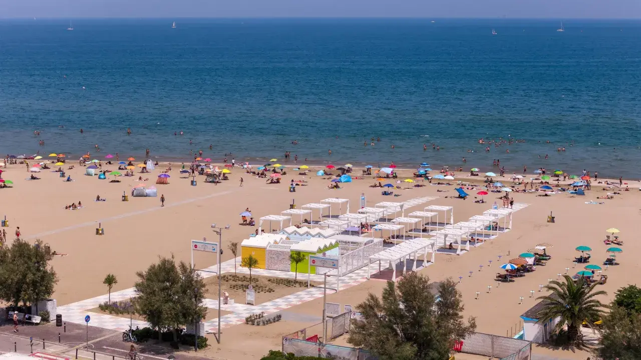 Una vivace spiaggia libera a Rimini, con bagnanti che si godono il sole e il mare sotto ombrelloni colorati.