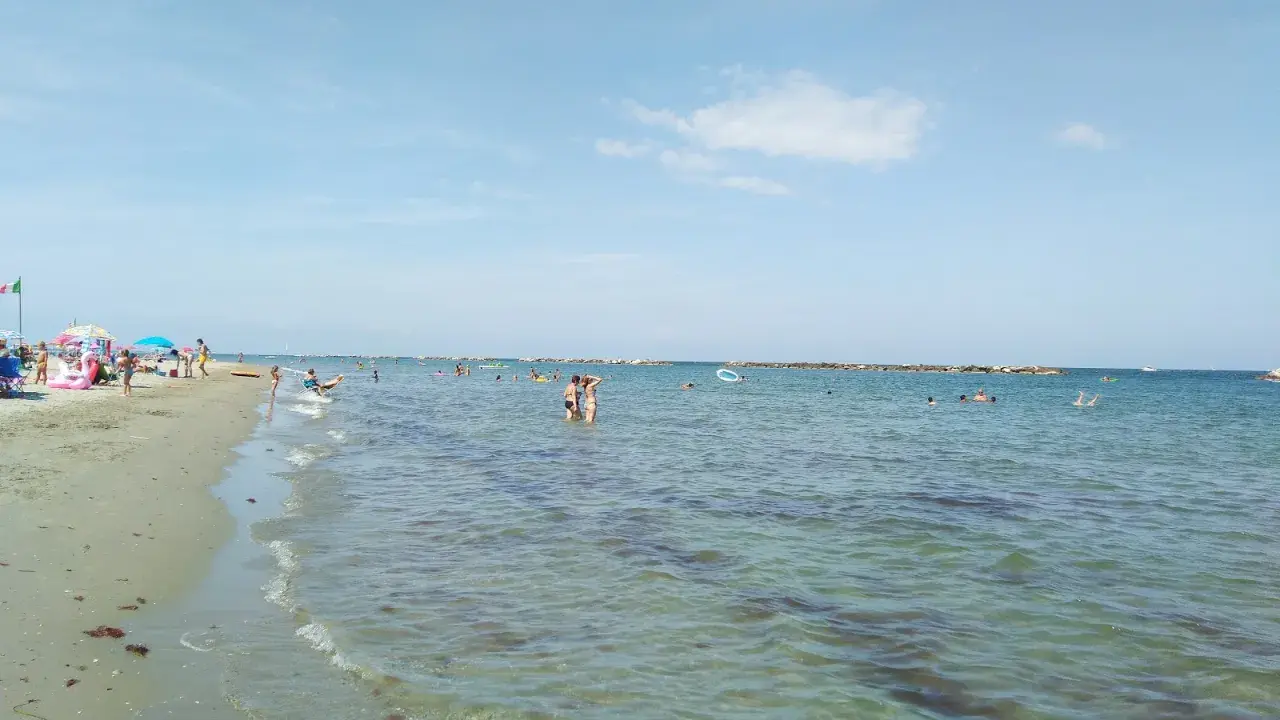 Gente che si gode il sole e il mare a Lido Adriano. Bambini giocano sulla sabbia, adulti nuotano e si rilassano nell'acqua cristallina.