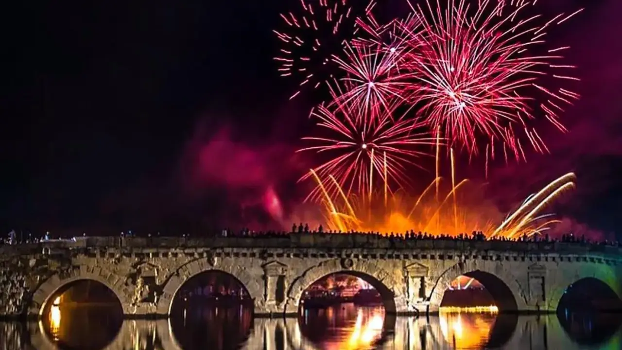 Fuochi d'artificio spettacolari illuminano il cielo notturno sopra un ponte storico, celebrando il capodanno in riviera romagnola.
