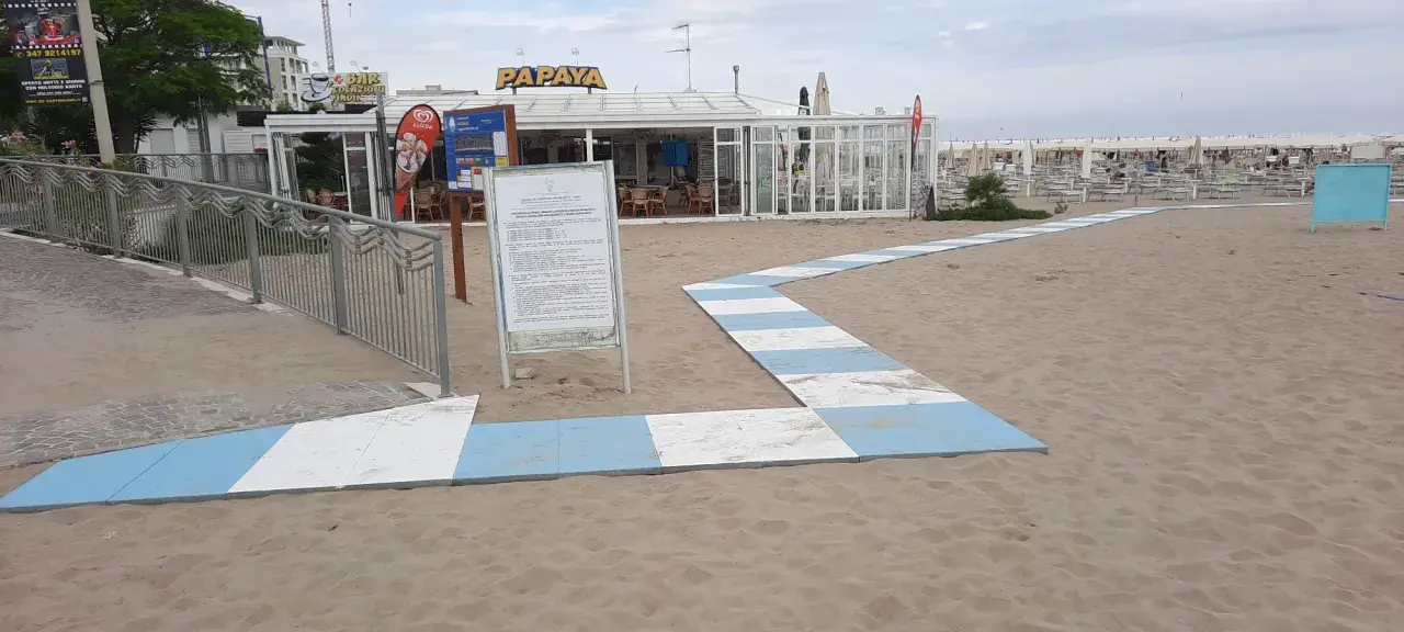 Percorso a strisce bianche e blu sulla sabbia del piazzale San Martino a Riccione, conduce al bar Papaya e alla spiaggia attrezzata.