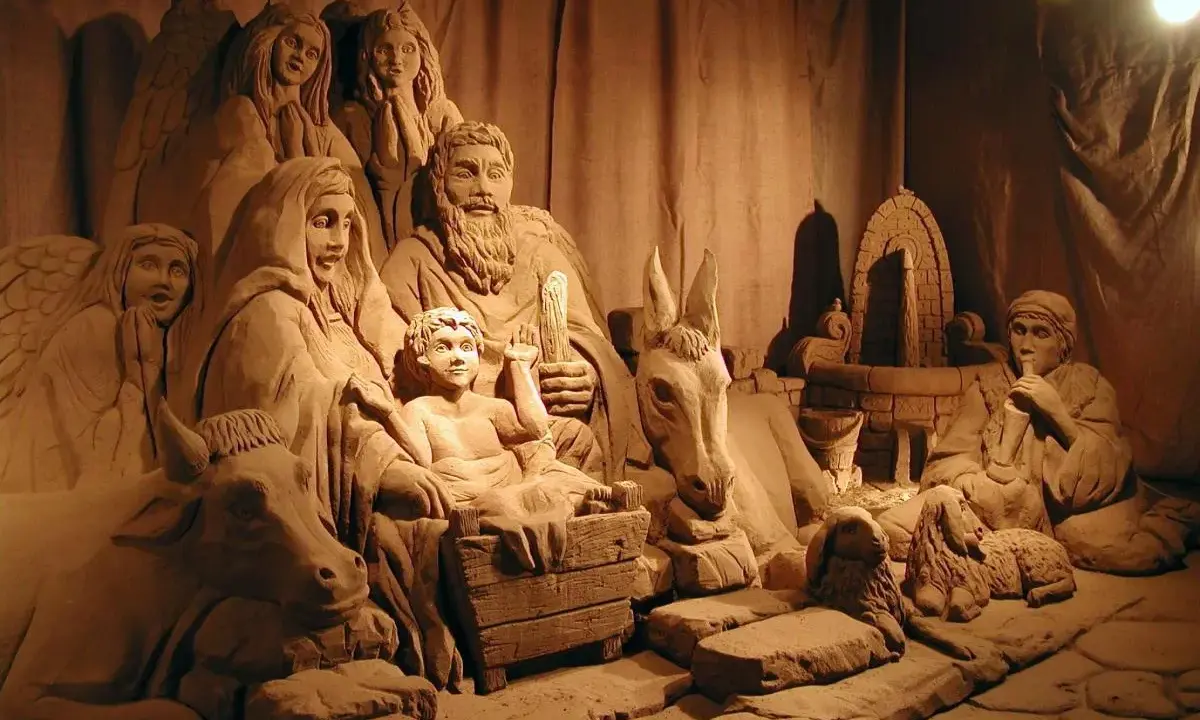 Un suggestivo presepe di sabbia a Rimini, con figure scolpite nella sabbia, tra cui angeli, la Sacra Famiglia, animali e un pastore.